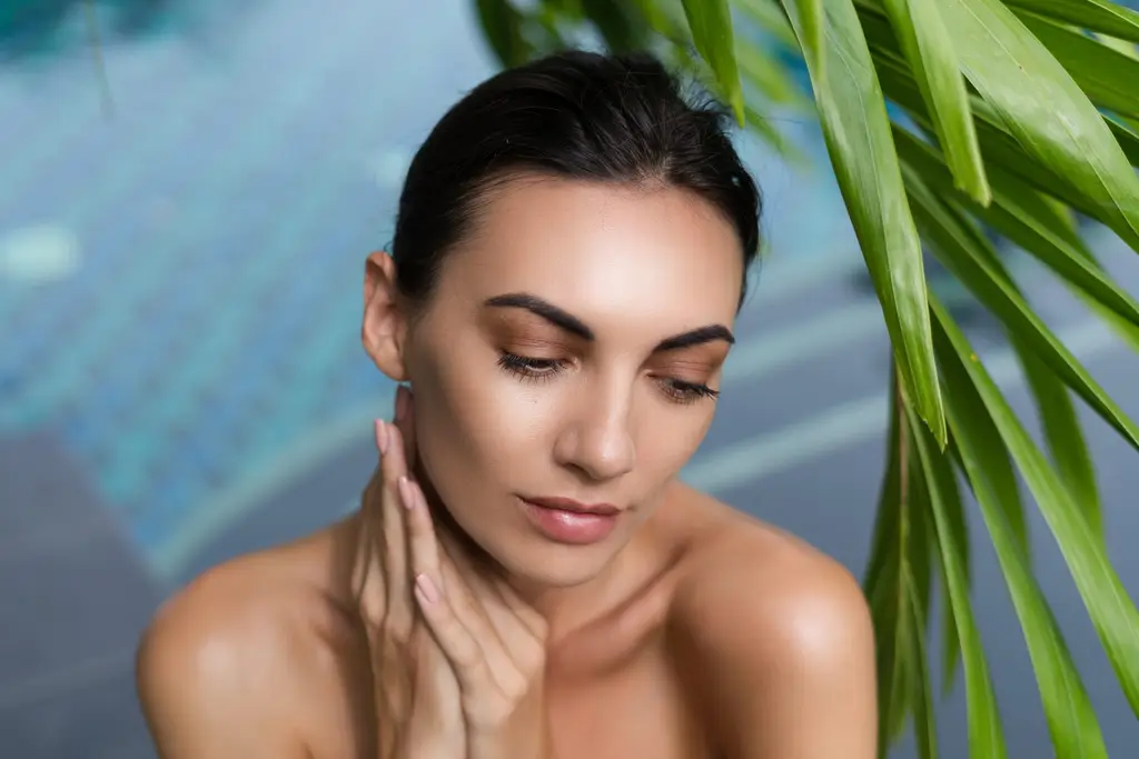 Woman with naturally glowing skin beneath palm leaves, skin revitalisation at Dulwich Natural Beauty London